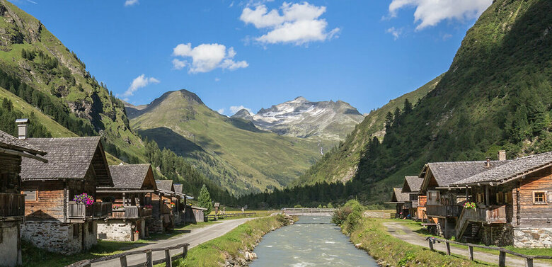 Klarer Tauernbach im Gschlösstal an einem Sommertag, mit traditionellen Almhütten entlang beider Ufer.