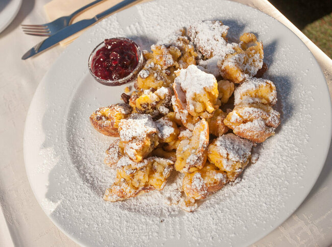 Kaiserschmarren mit Preiselbeeren in einem separaten Schüsselchen auf einem weißen Teller.