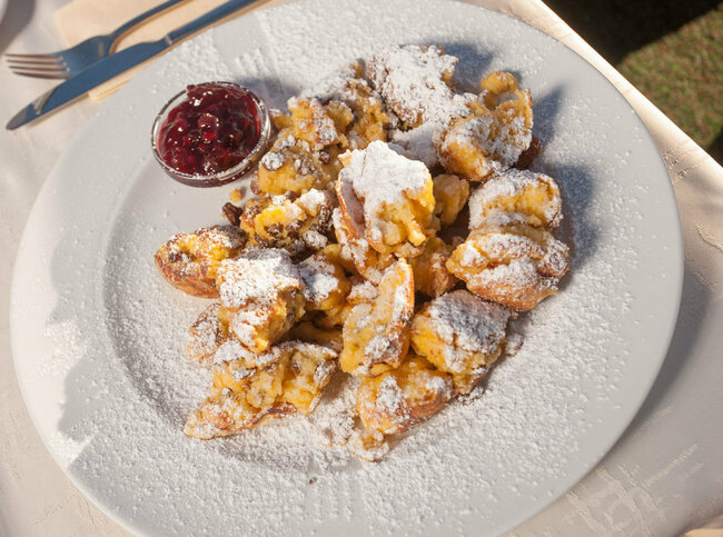 Kaiserschmarren mit Preiselbeeren in einem separaten Schüsselchen auf einem weißen Teller.