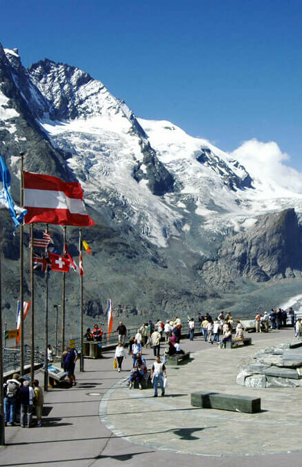 Weitblick von der Franz-Josefs-Höhe: Parkplatz mit wehenden Fahnen, dahinter die mächtige Pasterze und der imposante, schneebedeckte Großglockner.