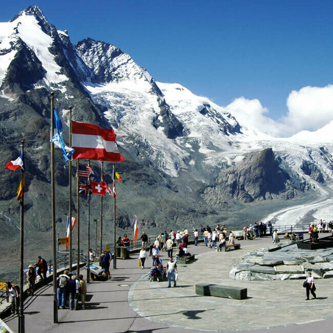 Weitblick von der Franz-Josefs-Höhe: Parkplatz mit wehenden Fahnen, dahinter die mächtige Pasterze und der imposante, schneebedeckte Großglockner.