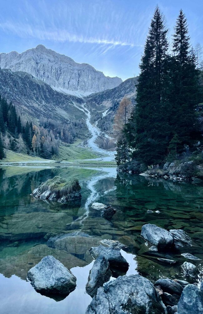 Glasklarer Klapfsee, der die mächtigen Felswände der Porze im Hintergrund widerspiegelt.
