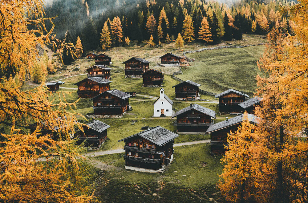 Almhüttendorf "Oberstalleralmen in Innvervillgraten" in herbstlicher Umgebung mit kleiner Kapelle im Zentrum; im Vordergrund goldgelbe Lärchen in Herbstfärbung