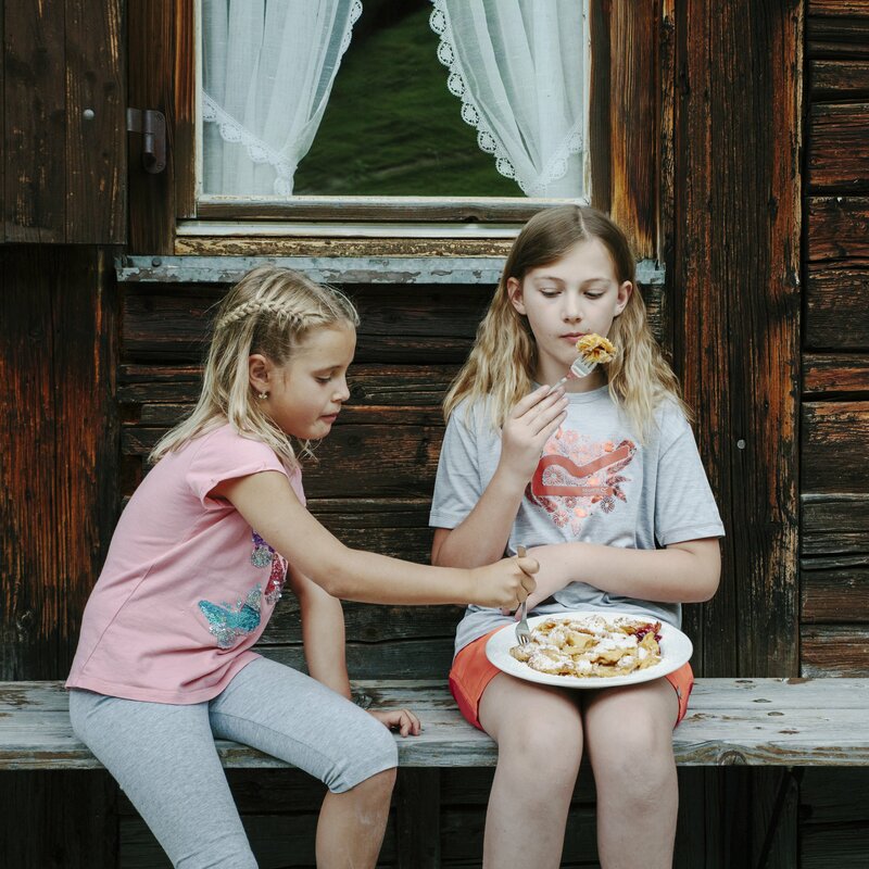 Zwei Kinder sitzen vor einer Hütte und genießen eine Nascherei