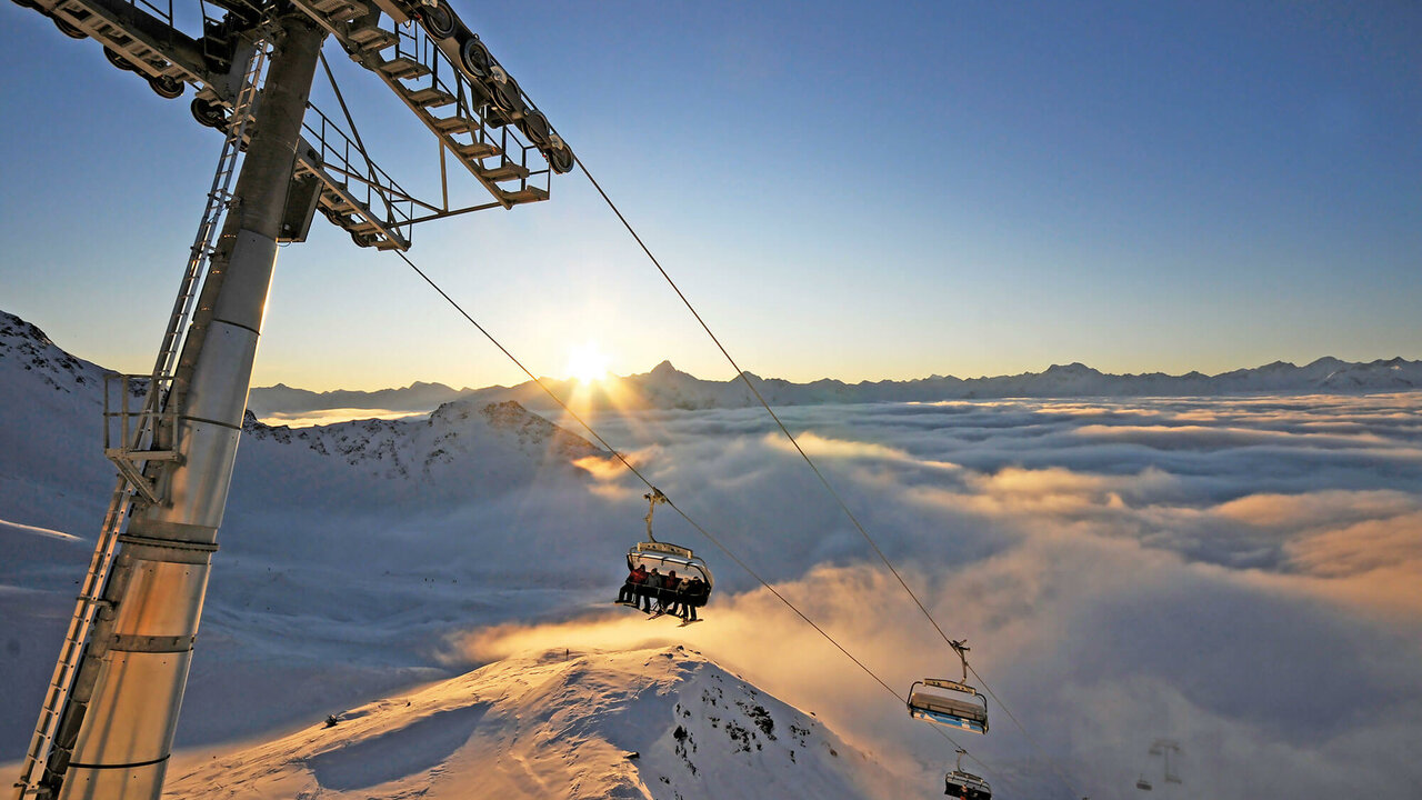 Großglockner Resort Kals Matrei Sessellift Der Sessellift im Sonnenuntergang im Großglockner Resort Kals Matrei über schneebedeckten Bergen.