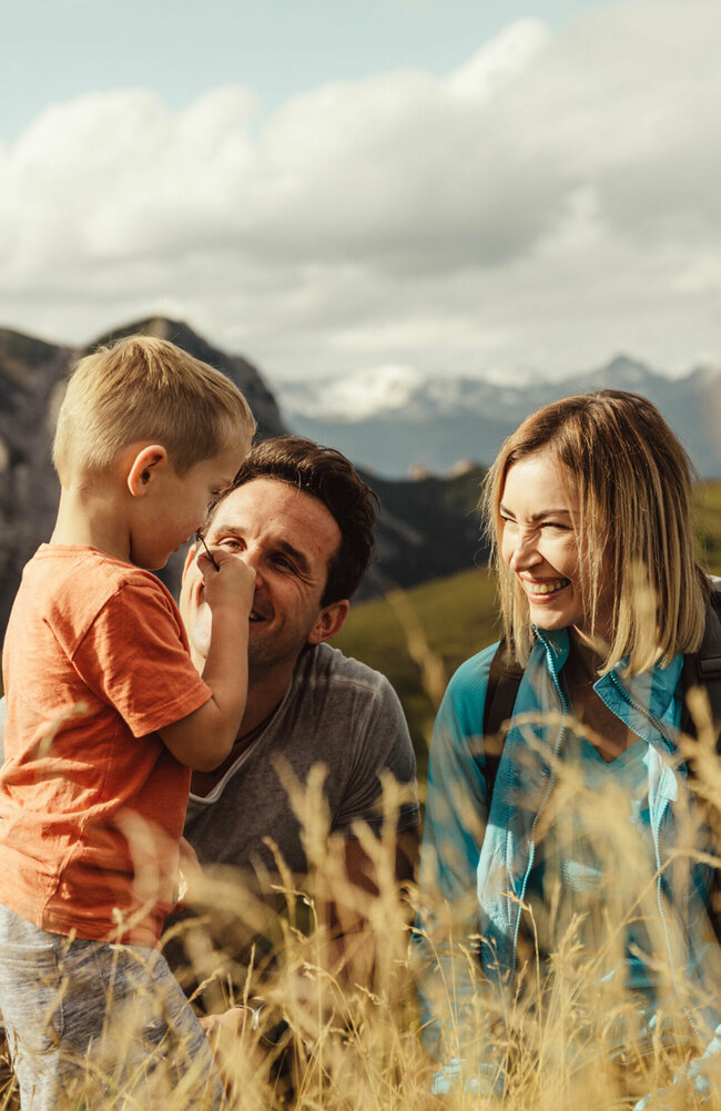 Zu sehen ist ein Elternpaar mit ihrem kleinen Sohn, die im hohen Gras entlang der Kindermeile am Golzentipp den Moment zu dritt genießen.