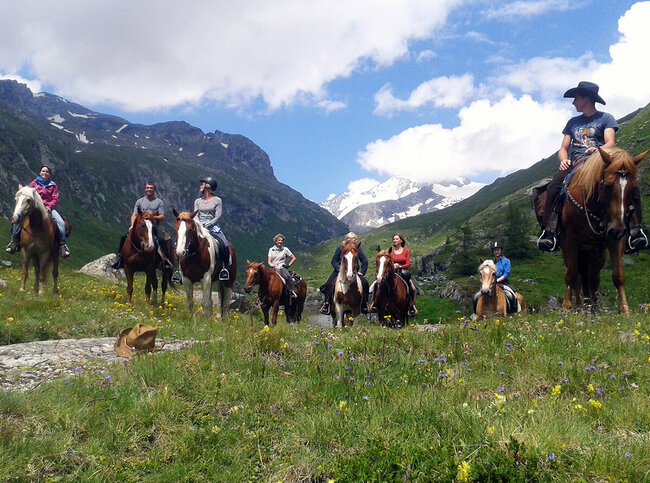 Reitbauernhof Acht Personen sitzen auf Pferden im Nationalpark Hohe Tauern vor einer Bergkulisse. Im Vordergrund liegt ein Cowboyhut auf dem Boden.