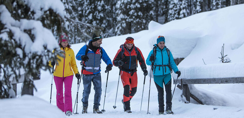 Winterwandern Kartitsch Zwei Pärchen wandern bunt gekleidet in verschneiter Winterlandschaft mit Stöcken ausgerüstet und Rucksack auf einem Winterwanderweg.