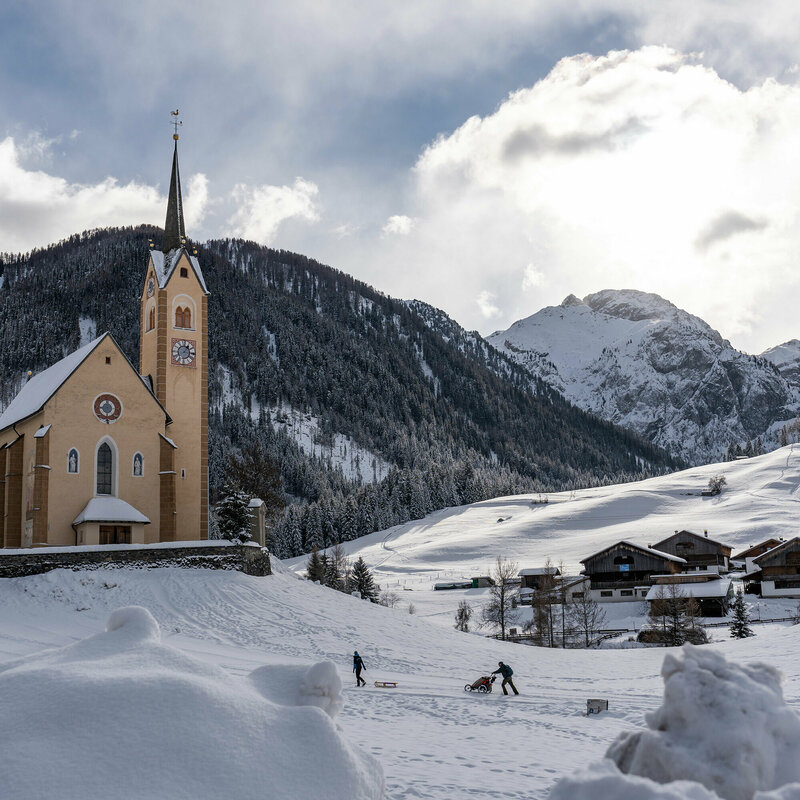 Kartitscher Pfarrkirche im Winter umgeben von schneebedeckten Feldern und den Karnischen Alpen im Hintergrund