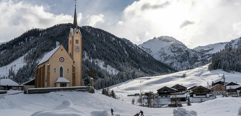 Kartitscher Pfarrkirche im Winter umgeben von schneebedeckten Feldern und den Karnischen Alpen im Hintergrund
