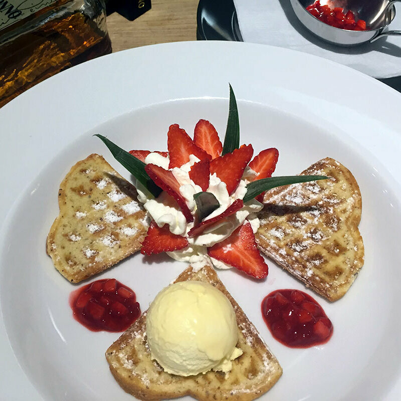 Drei Waffeln mit Erdbeeren, Sahne und einer Eiskugel auf einem Teller.
