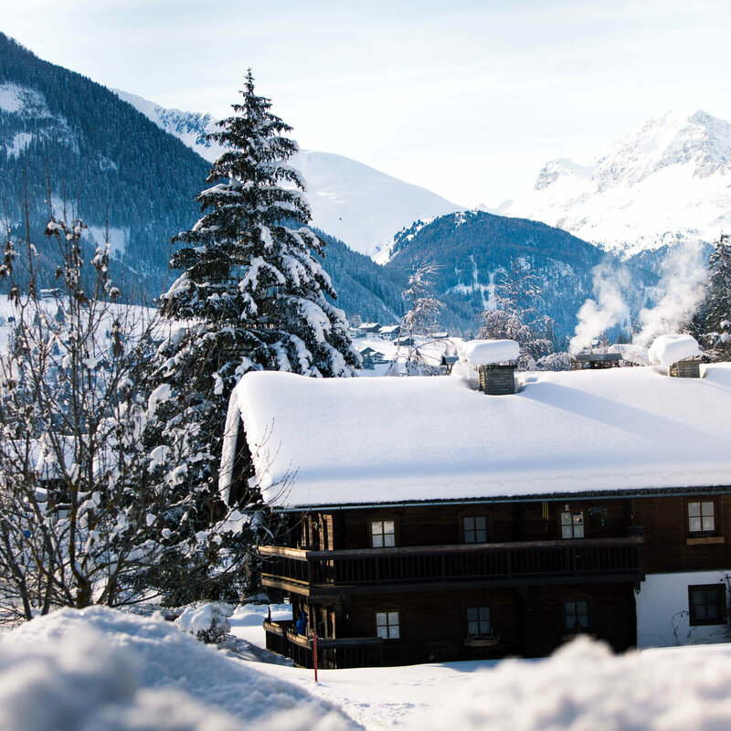 Blick auf eine verschneite, dunkle Holzhütte im Winter im Defereggental.