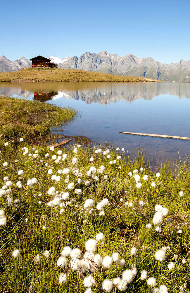 Der Zupalsee spiegel in seinem klaren Wasser die Zupalsee Hütte und die umliegende Bergwelt wider.