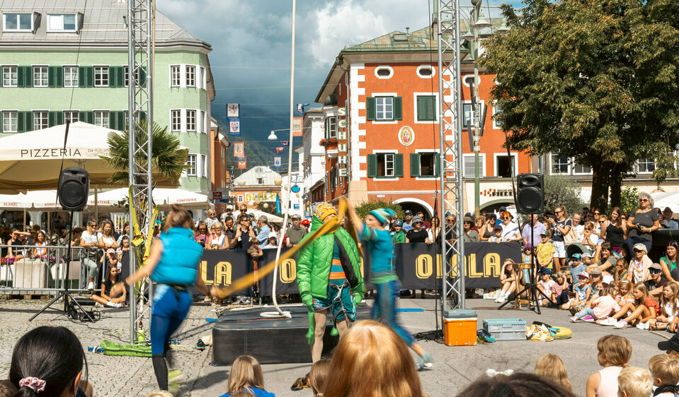 Drei Artistinnen am Olala 2025, zwei davon hüllen die dritte in dicke Winterkleidung, rundherum stehen und sitzen begeisterte Zuseherinnen und Zuseher.