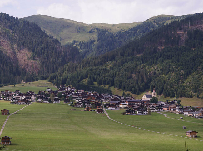 Ansicht eines Haufendorfes im Sommer von Süden aus. Wolken schatten das Sonnenlicht leicht ab.