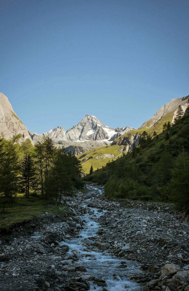 Blick auf einen kleinen Bach mit Grossglockner im Hintergrund an einem herrlichen Tag mit blauem Himmel.
