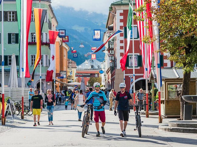 Zwei Mountainbiker schieben ihre Räder durch die mit Fahnen dekorierte Innenstadt von Lienz.