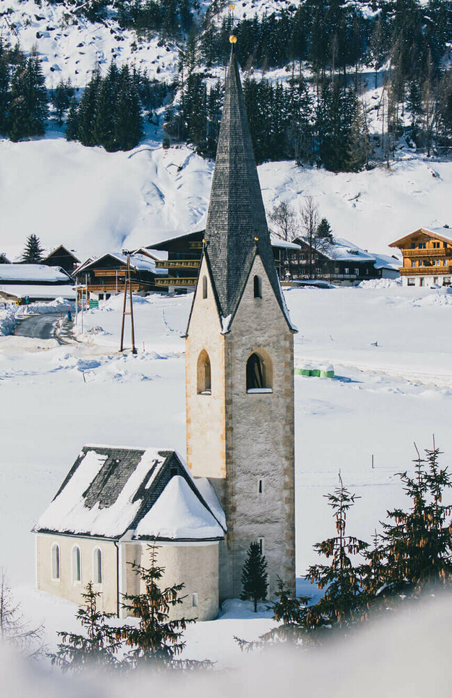 Blick auf die Kals Kirche mit schwarzem Dach in einer schneebedeckten Winterlandschaft.