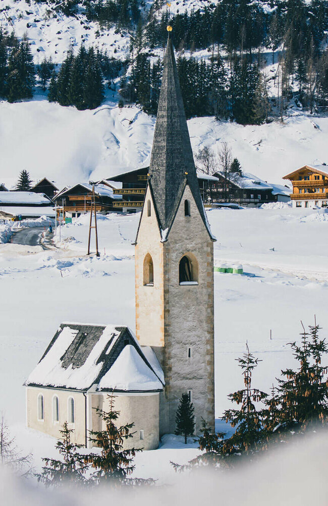 Blick auf die Kals Kirche mit schwarzem Dach in einer schneebedeckten Winterlandschaft.