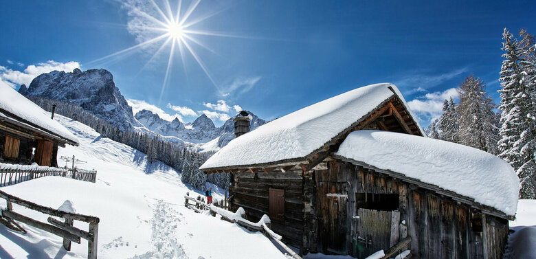 Eine tief verschneite Hütte in den sonnigen Dolomiten, blauer Himmel, weißer Schnee.