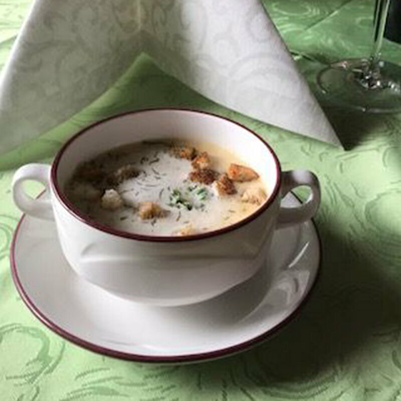 Eine Portion Knoblauchcreme-Suppe mit Croutons und Kräutern auf einem Tisch mit einer grünen Tischdecke.