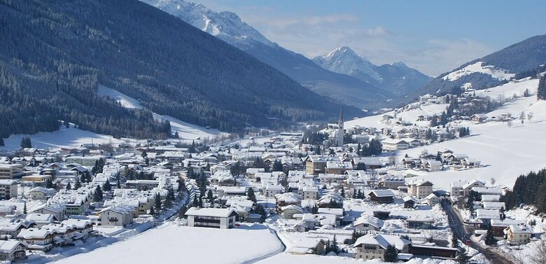 Ortsansicht von Sillian mit verschneiter Winterlandschaft und Blick auf die Sextener Dolomiten im Hintergrund.