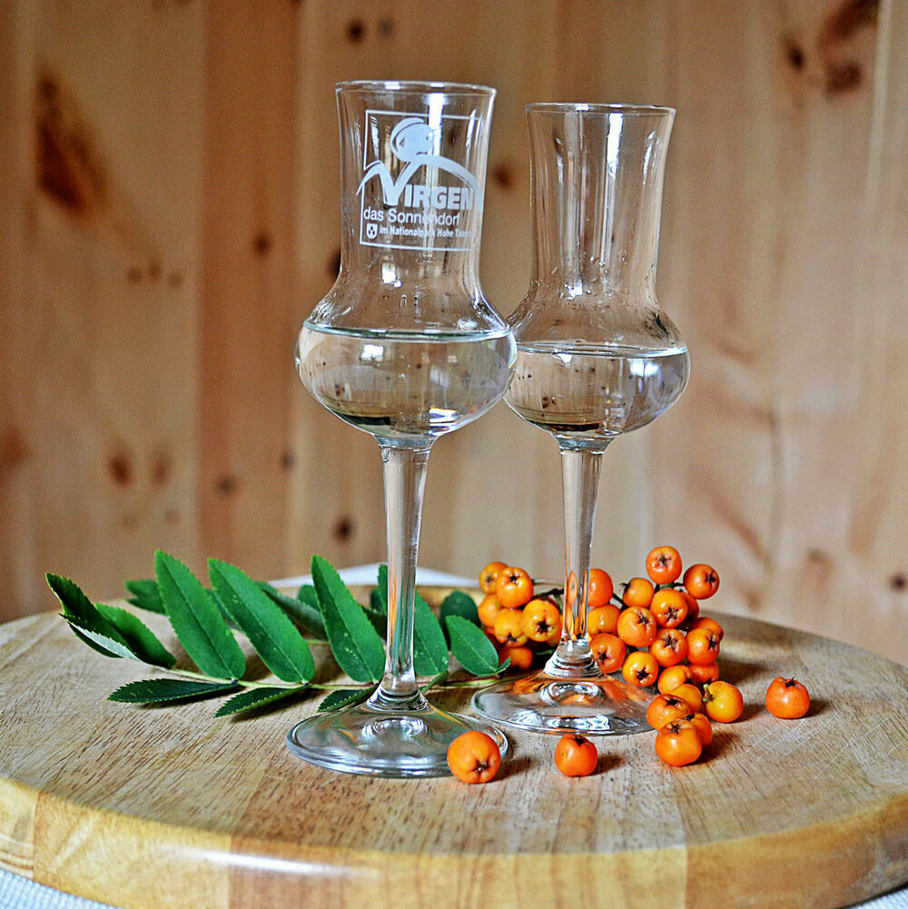 Zwei Gläser Vogelbeerschnaps auf einem Holzbrett, mit einigen Vogelbeeren daneben.