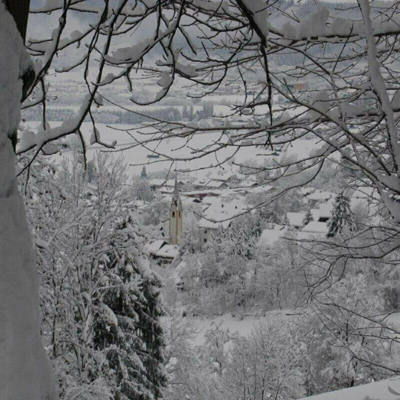 Blick auf das verschneite Nussdorf mit Kirche, aus dem Wald heraus fotografiert.