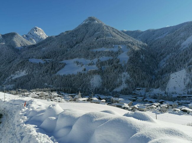 Ortsteil der Ortschaft Abfaltersbach im tief verschneiten Winter. Im Hintergrund bewaldete Hänge.