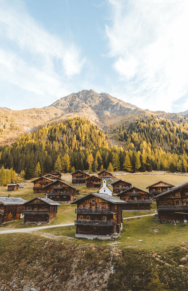 Die Hüttenansammlung mit kleiner Kapelle in der Mitte der Oberstalleralm in herbstlicher Umgebung mit verfärbten Wäldern.