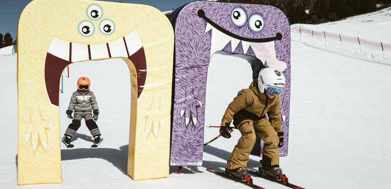 Zwei Kinder fahren auf Skiern durch bunte Monstertore auf der Funslope im Skigebiet Zettersfeld in Osttirol und genießen spielerischen Skispaß im Schnee.