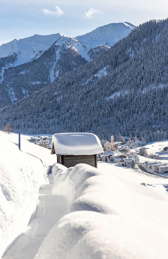 Man sieht Kartitsch in frisch verschneitem Zustand. Ein frisch bereiteter Winterwanderweg führt durch die malerische Szenerie des ersten Winterwanderdorfs Österreichs.
