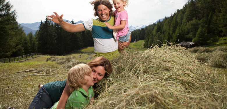 Eine Familie macht Urlaub am Bauernhof und spielt im Heu auf einer Wiese.