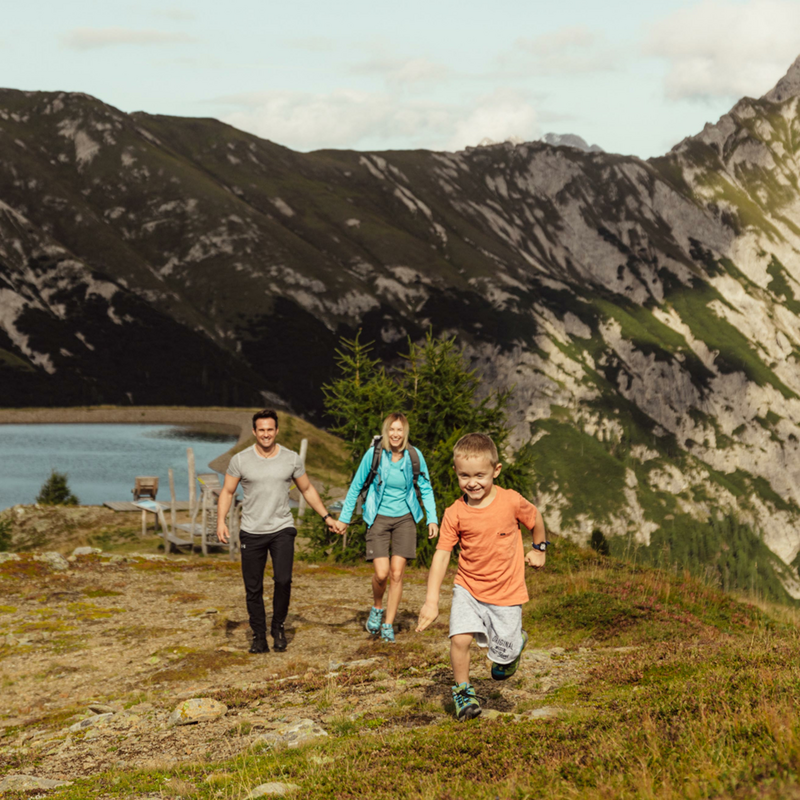 Ein kleiner Junge in kurzen, hellblauen Hosen und orangem T-Shirt entfernt sich mit seinen im Hintergrund gehenden Eltern vom Speichersee am Golzentipp.