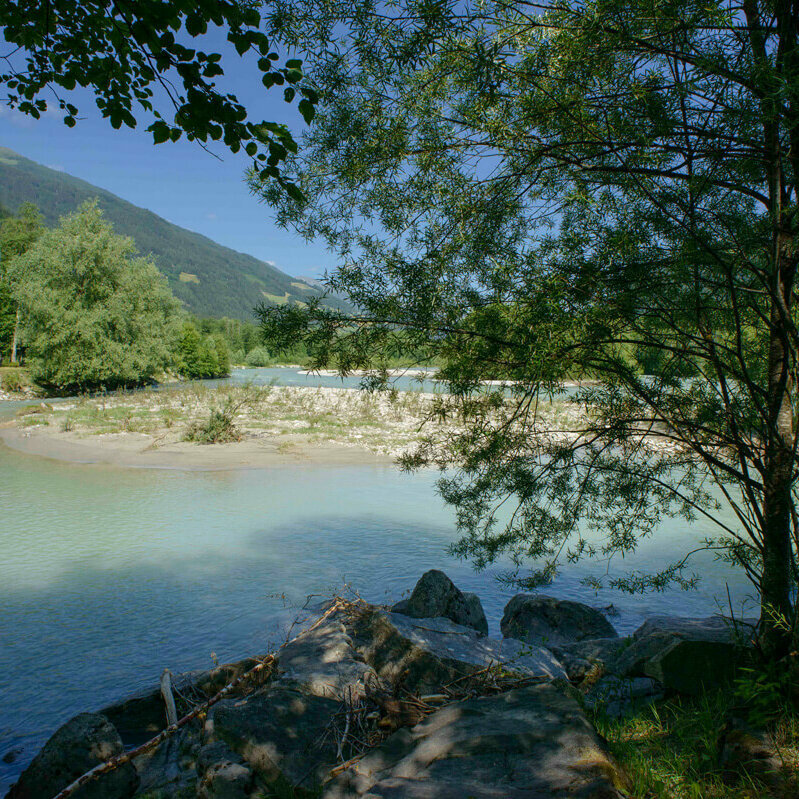 Untere Isel in Oberlienz Das türkis-blaue Wasser der unteren Isel in Oberlienz. In der Mitte ist eine kleine Sandbank. Am Ufer wachsen viele grüne Bäume.