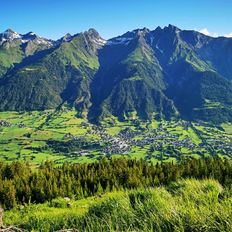 Panoramaaussicht auf die Gemeinde Virgen mit saftig grünen Wiesen und Wäldern drum herum. Auf den Berggipfeln liegt noch vereinzelt Schnee.