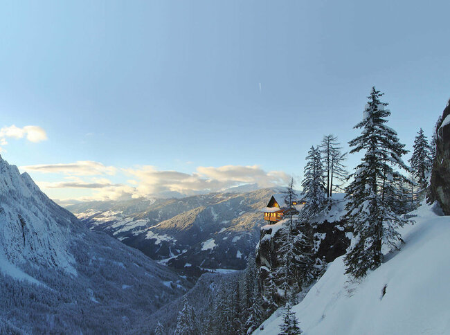 Panoramablick auf die beleuchtete Dolomitenhütte im Winter. Die Landschaft ist tief verschneit.