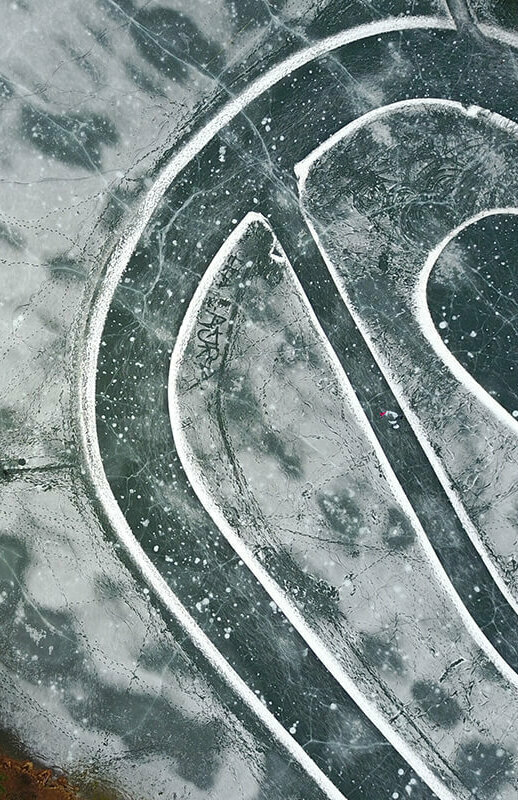 Der Eislaufplatz am Tristachersee aus der Vogelperspektive fotografiert. Eine ovale Spur ist auf dem Eis.