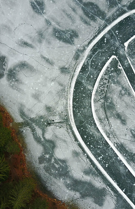 Der Eislaufplatz am Tristachersee aus der Vogelperspektive fotografiert. Eine ovale Spur ist auf dem Eis.