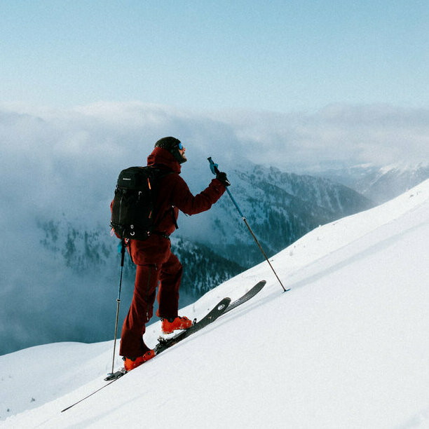 Zwei Skitourensportler erklimmen im Gleichschritt auf ihren Tourenskiern einen mittelsteilen Berghang an einem Schönwettermorgen. Dahinter verdeckt zäher Hochnebel einen Teil der Berge.