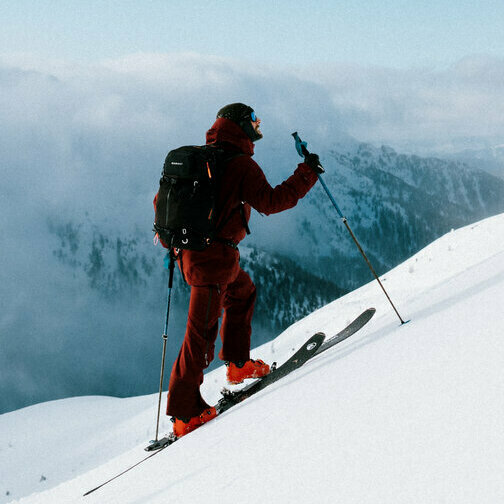 Zwei Skitourensportler erklimmen im Gleichschritt auf ihren Tourenskiern einen mittelsteilen Berghang an einem Schönwettermorgen. Dahinter verdeckt zäher Hochnebel einen Teil der Berge.