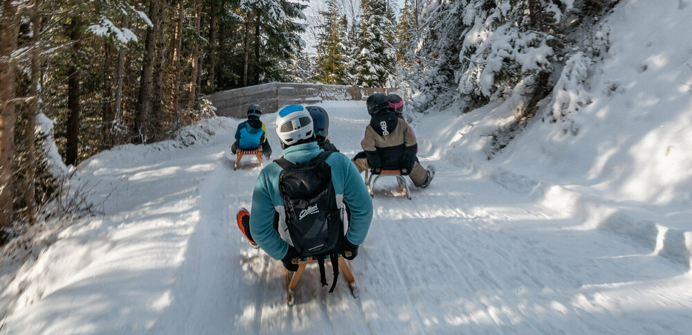 Eine Familie in Skianzügen rodelt auf ihren Schlitten talwärts auf der Rodelbahn im Winkeltal in Außervillgraten, Osttirol.
