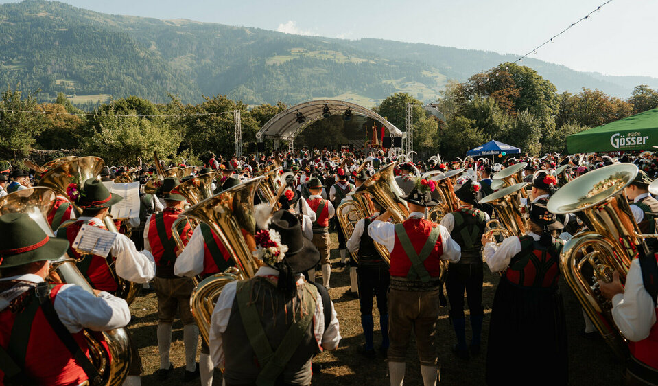 Unzählige Musikant:innen spielen gemeinsam bei der Messe im Klostergarten. Im Hintergrund sieht man Berge.