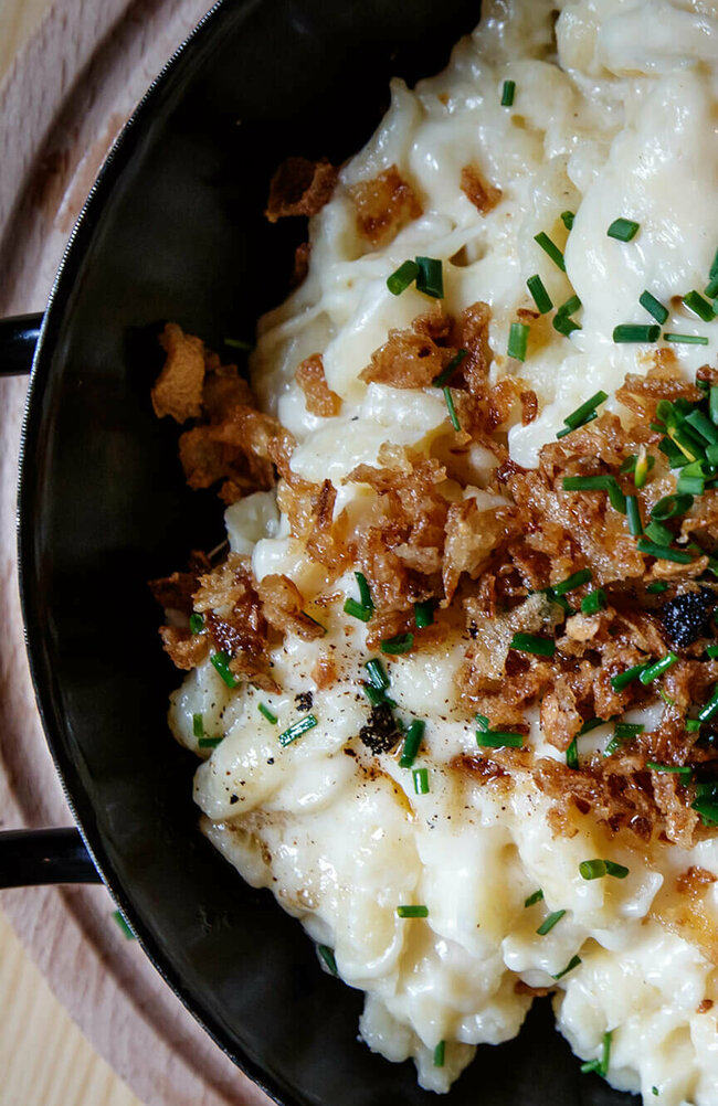 Käsespätzle mit gerösteten Zwiebeln traditionell in einem kleinen, schwarzen Eisenpfännchen