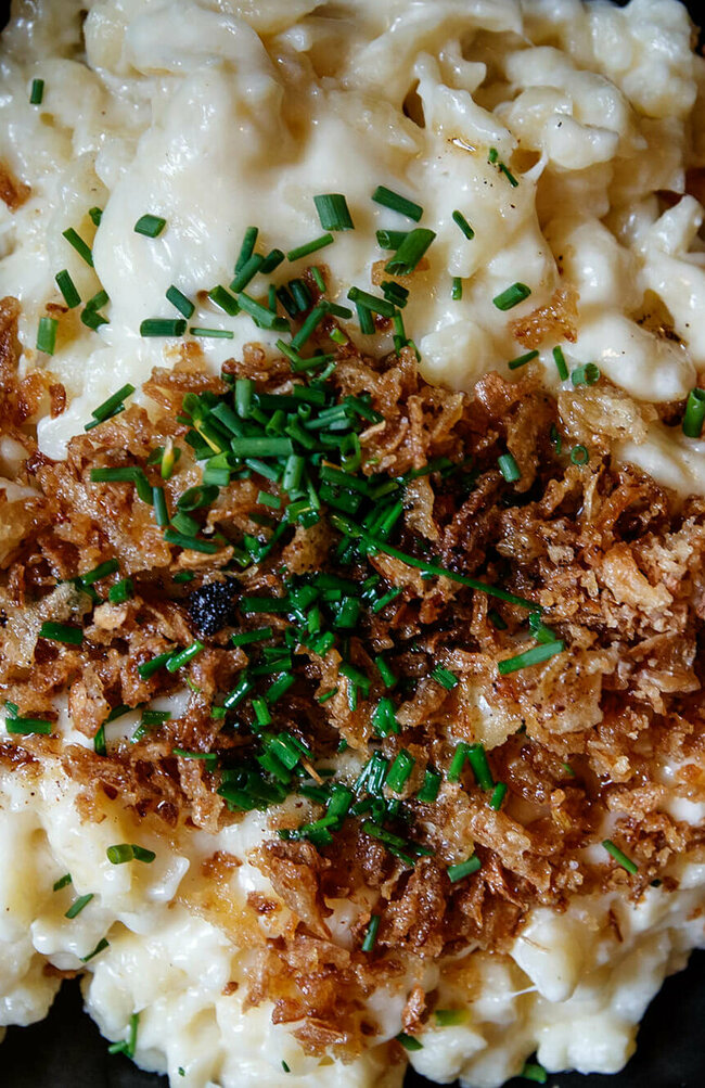 Käsespätzle mit gerösteten Zwiebeln traditionell in einem kleinen, schwarzen Eisenpfännchen