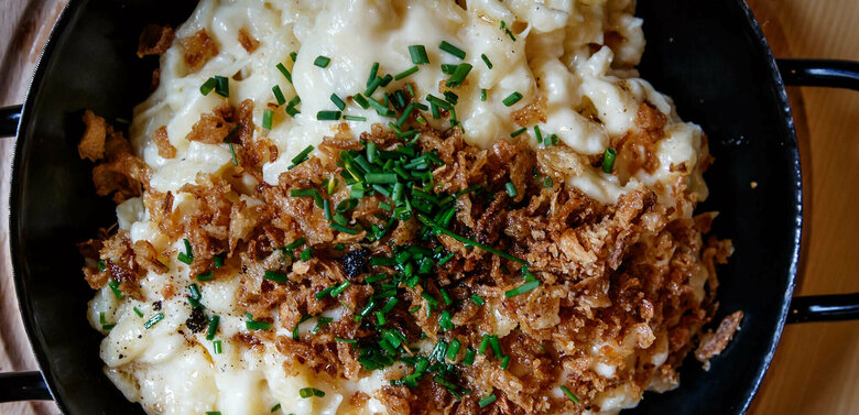 Käsespätzle mit gerösteten Zwiebeln traditionell in einem kleinen, schwarzen Eisenpfännchen