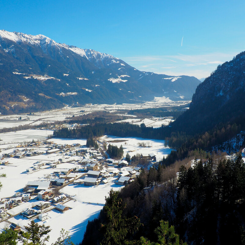 Luftaufnahme der Gemeinde Lavant im Winter. Rechts im Bild zu sehen ist die Kirche St. Ulrich.
