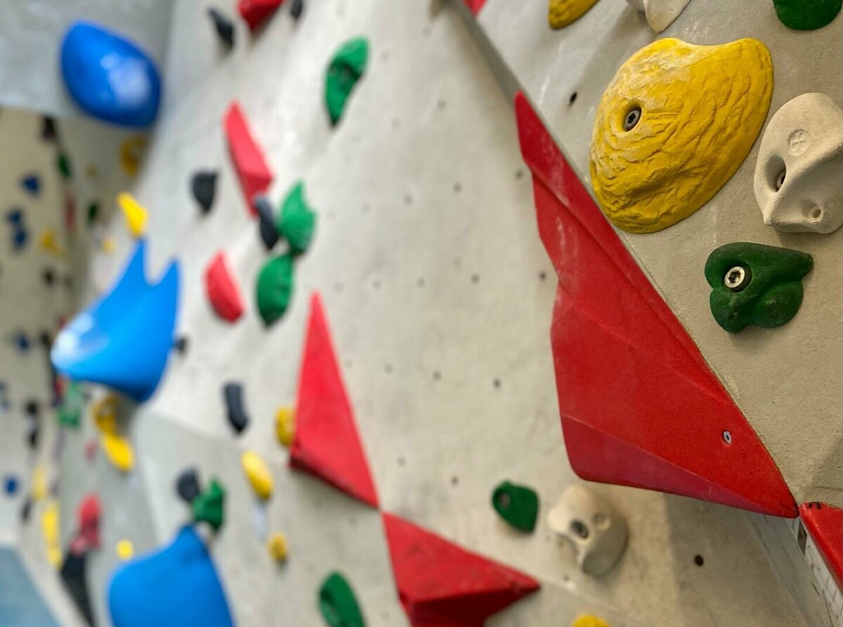 Verschiedene, bunte Boulderelemente an einer grauen Kletterwand im Boulderbox Freizeitzentrum in Gries.