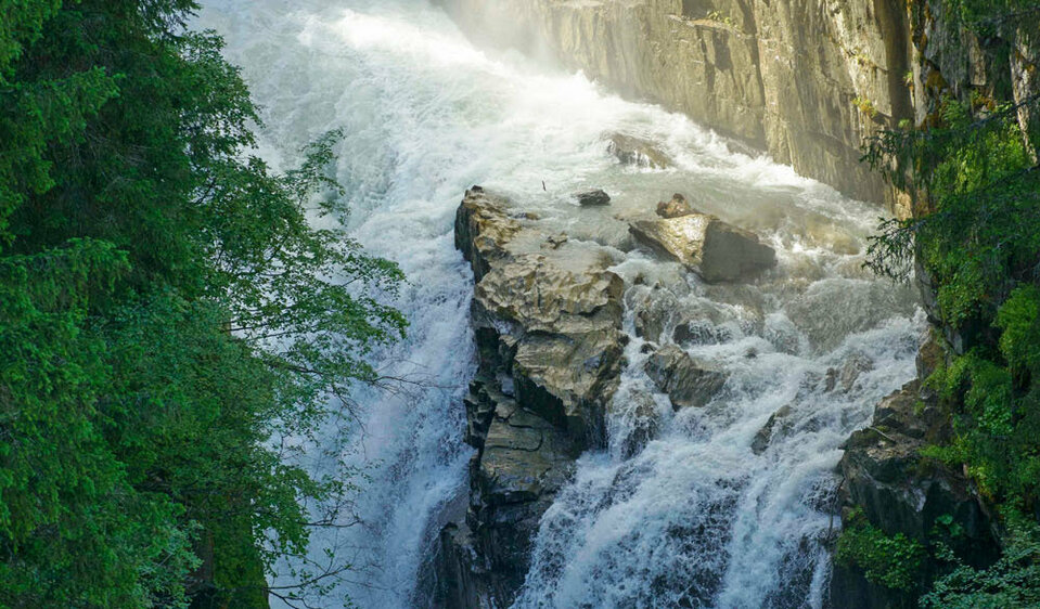Foto des Wasserfalls in der Gloschlucht, welcher von grünen Bäumen umgeben ist. 