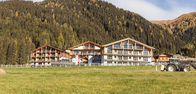 Die drei gleich aussehenden Häuser des Almfamilyhotel Scherers. Davor liegt eine grüne Wiese und dahinter erhebt sich ein bewaldeter Hang.